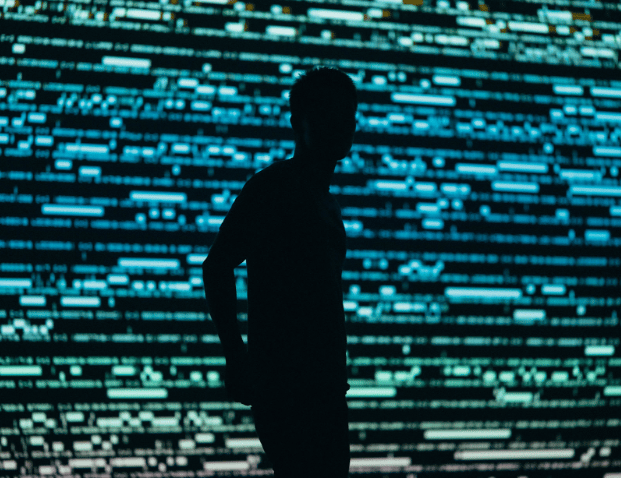 Silhouette of man standing in front of computer screen